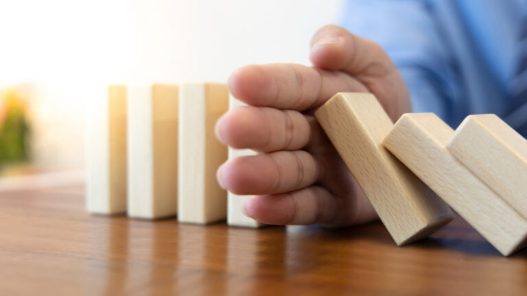 An image of someone preventing blocks from falling down in a domino effect. Blog article on vendor risk management strategies.